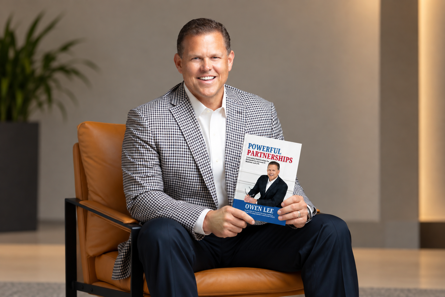 Owen Lee seated in an armchair holding a copy of Powerful Partnerships