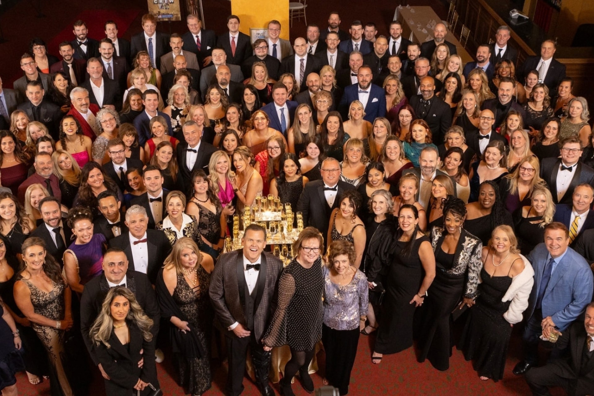 Success Mortgage Partners team at a black-tie gala, roughly eighty guests in formal wear gathered around a tiered tower of champagne flutes